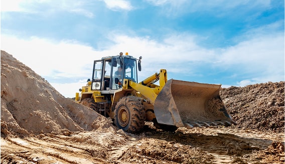 Yellow front-end loader with a full bucket between dirt piles.